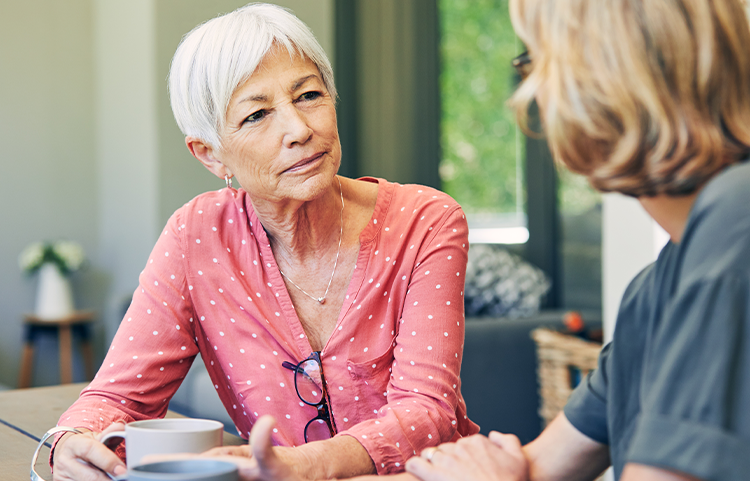 An older woman is sitting, having coffee with a friend.